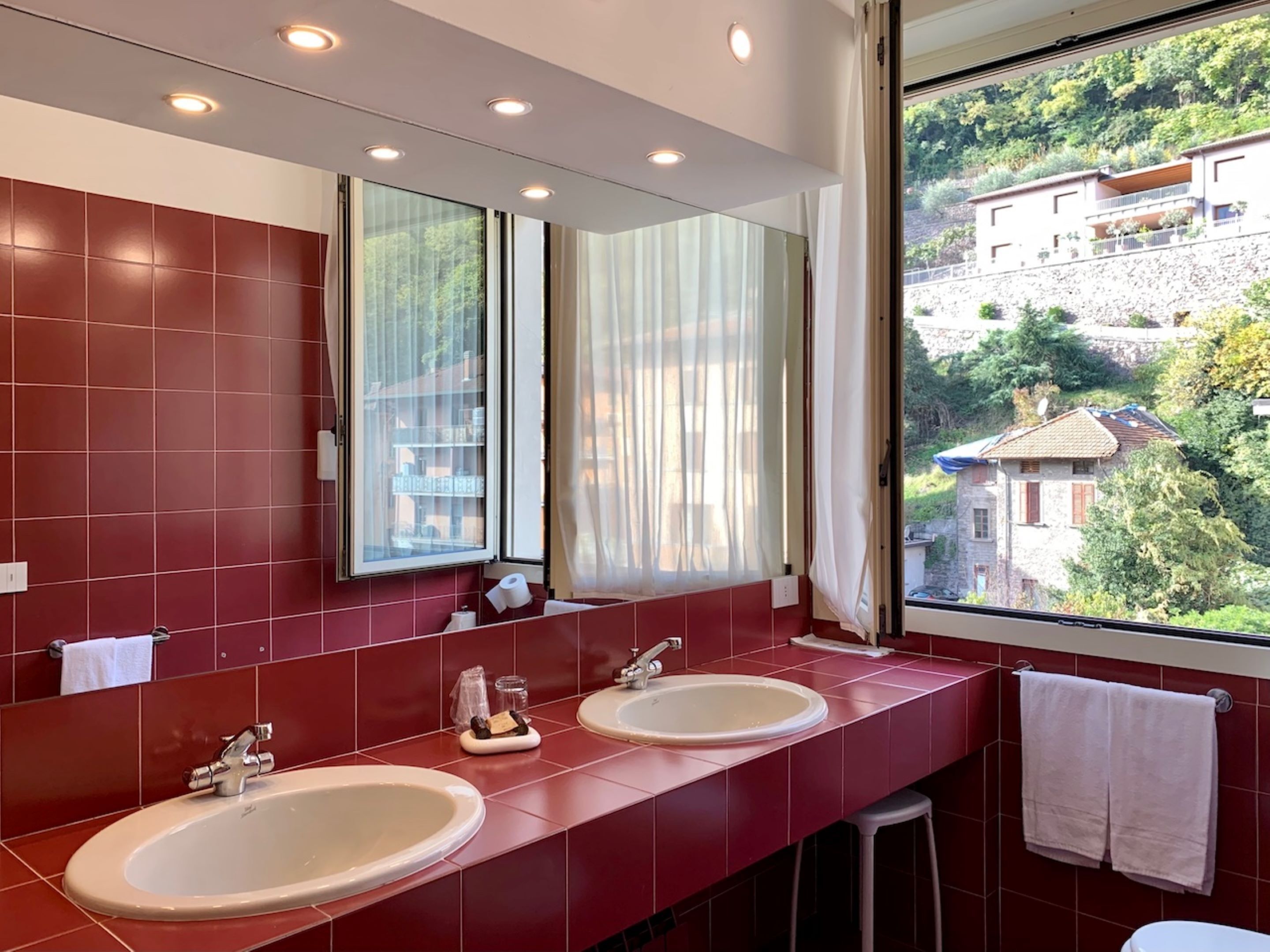 Un baño moderno con dos lavamanos, un espejo grande y vistas a una ladera a través de un ventanal amplio.