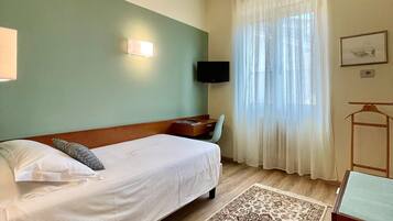 Una camera d'albergo con un letto, un comodino, una scrivania, una sedia, una televisione, una finestra con tende e un tappeto decorato.