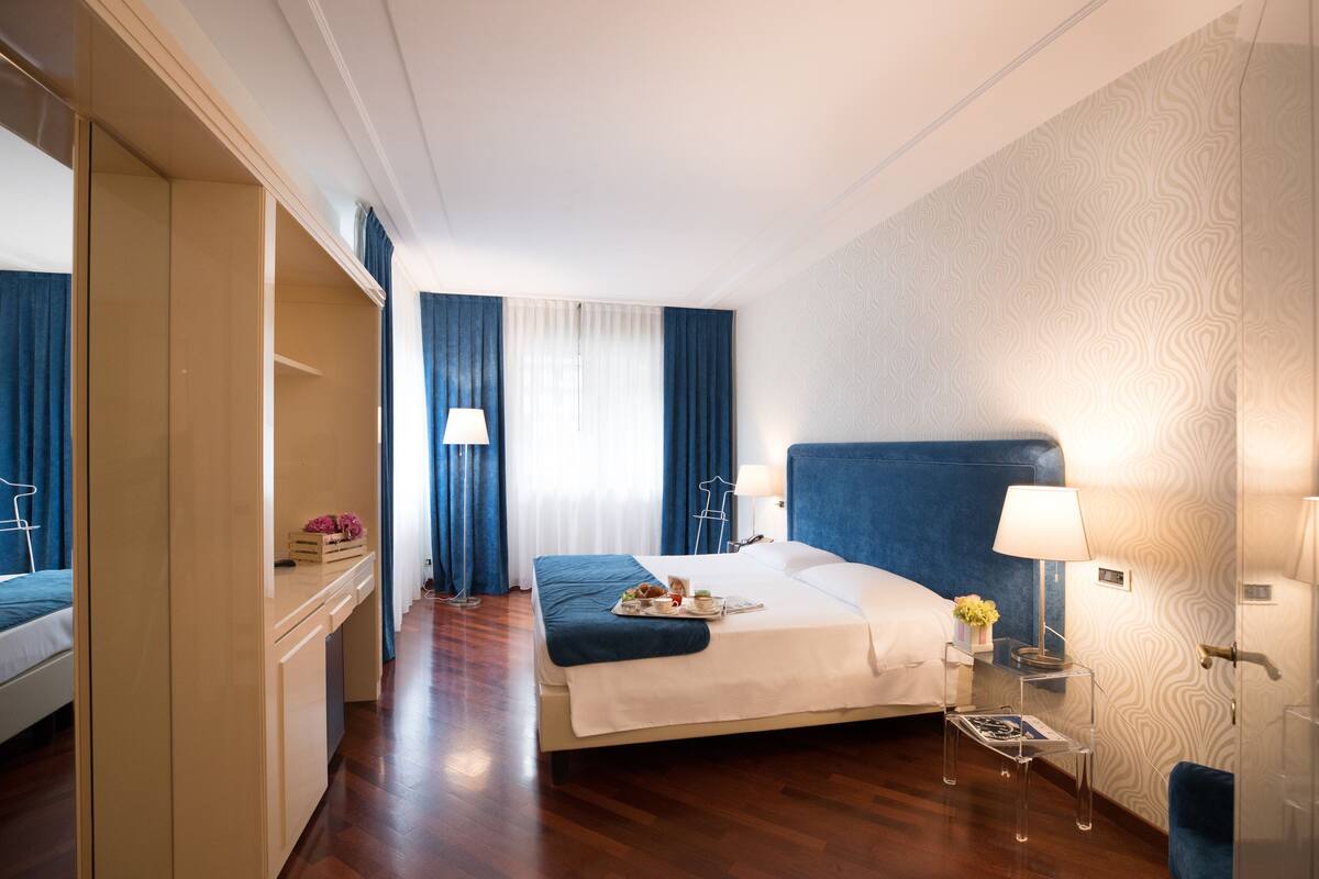 Een hotelkamer met een bed, nachtkastjes, een kledingkast en een raam met gordijnen.