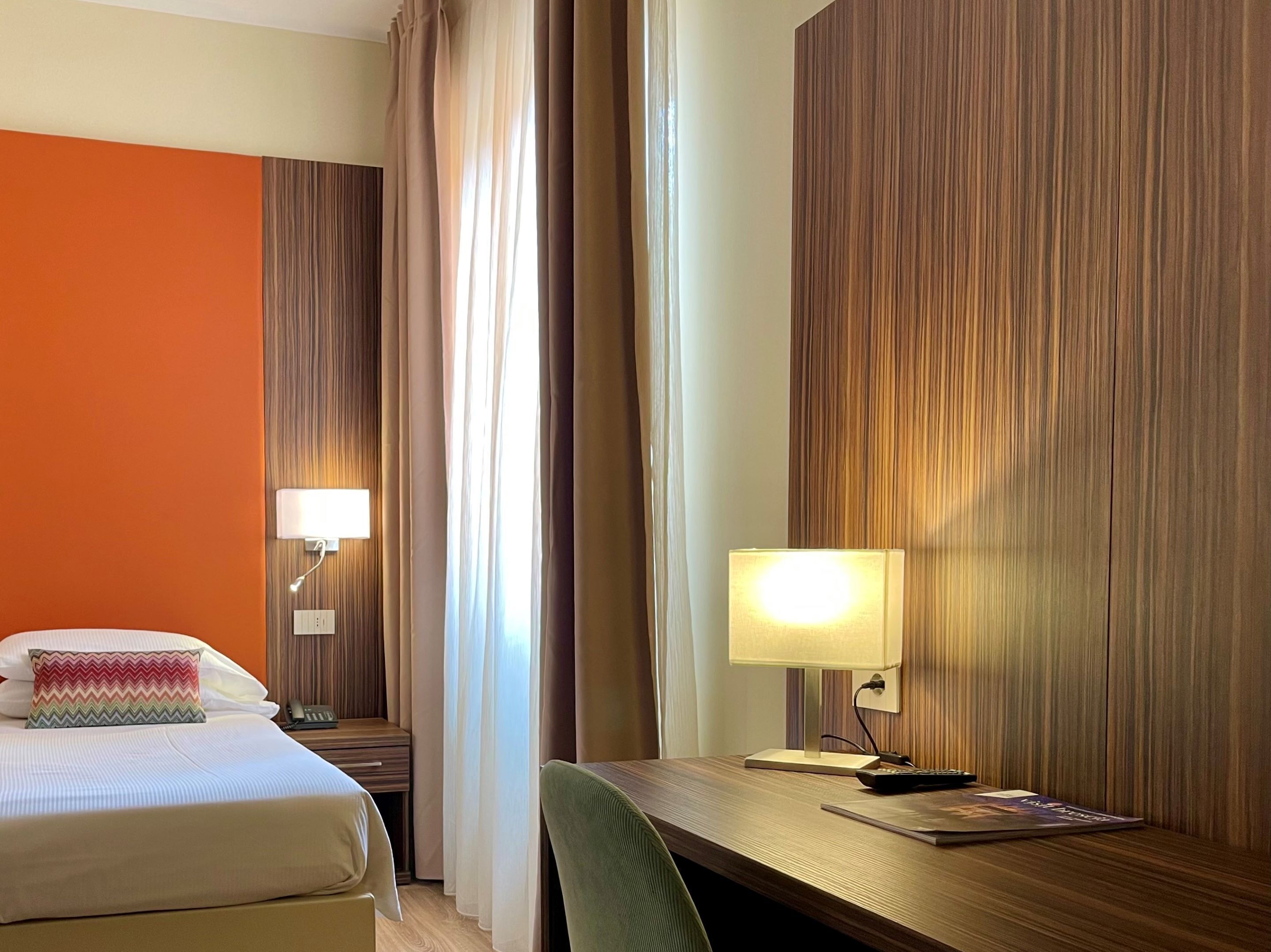 Une chambre d’hôtel avec un lit, un bureau, une lampe et une table de chevet.