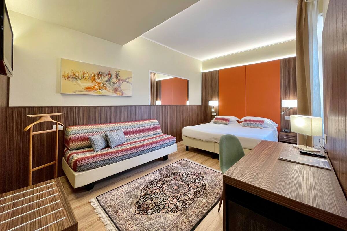 Een hotelkamer met een bank, een bed, een bureau en een vloerkleed.