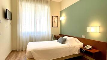 Une chambre d’hôtel avec un lit, un bureau, un téléphone, un tableau au mur et une fenêtre avec des rideaux.