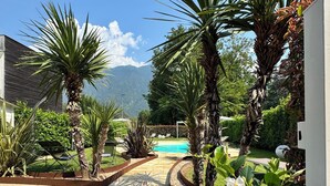 Un jardín ajardinado con un sendero de piedra que conduce a una piscina, rodeado de diversas plantas y una montaña al fondo.