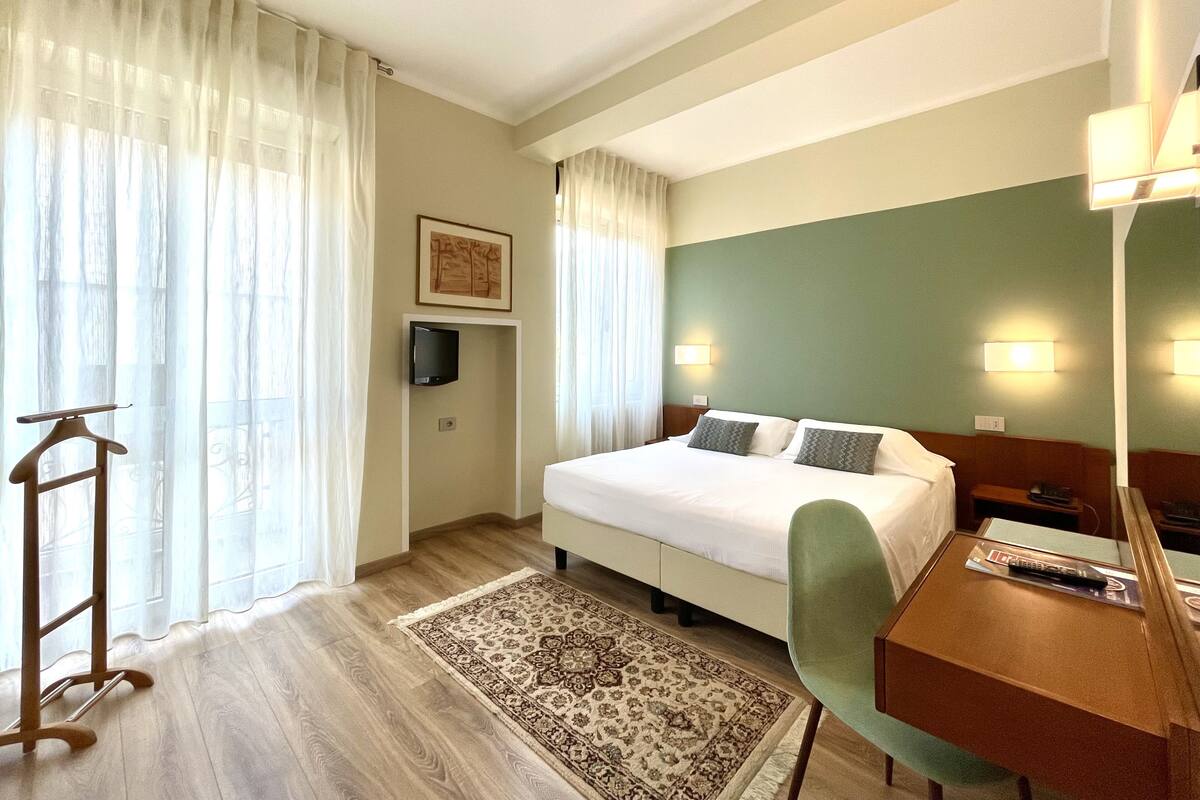 Een hotelkamer met een bed, een bureau, een stoel, een aan de muur bevestigde televisie en een kamerkleed met een patroon.