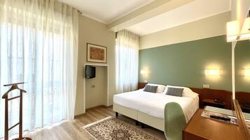 Een hotelkamer met een bed, een bureau, een stoel, een aan de muur bevestigde televisie en een kamerkleed met een patroon.