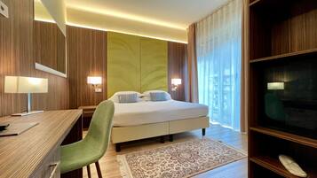 A hotel room with a bed, desk, chair, TV, and a large window with curtains.