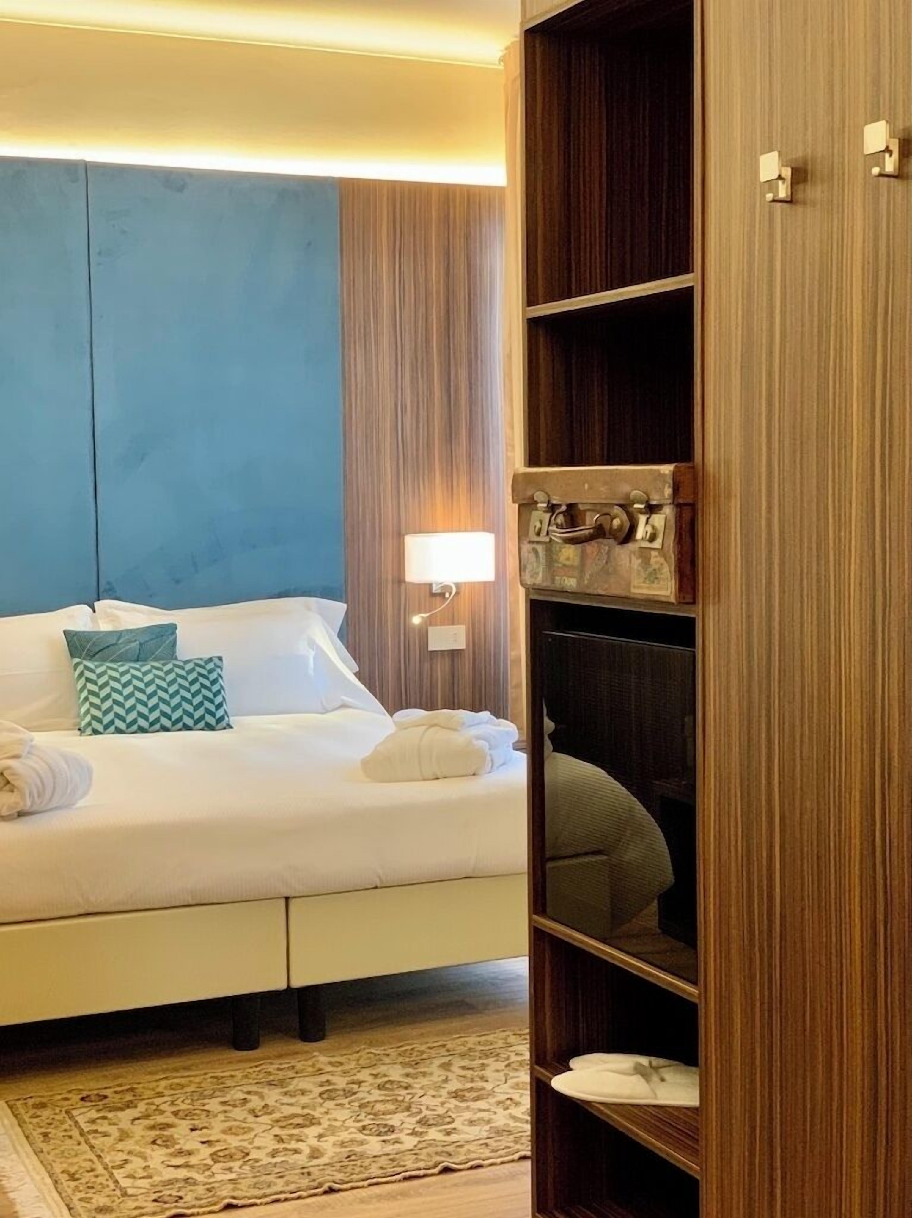 Una cama bien hecha con almohadas, una lámpara de noche y un armario de madera con estantes.