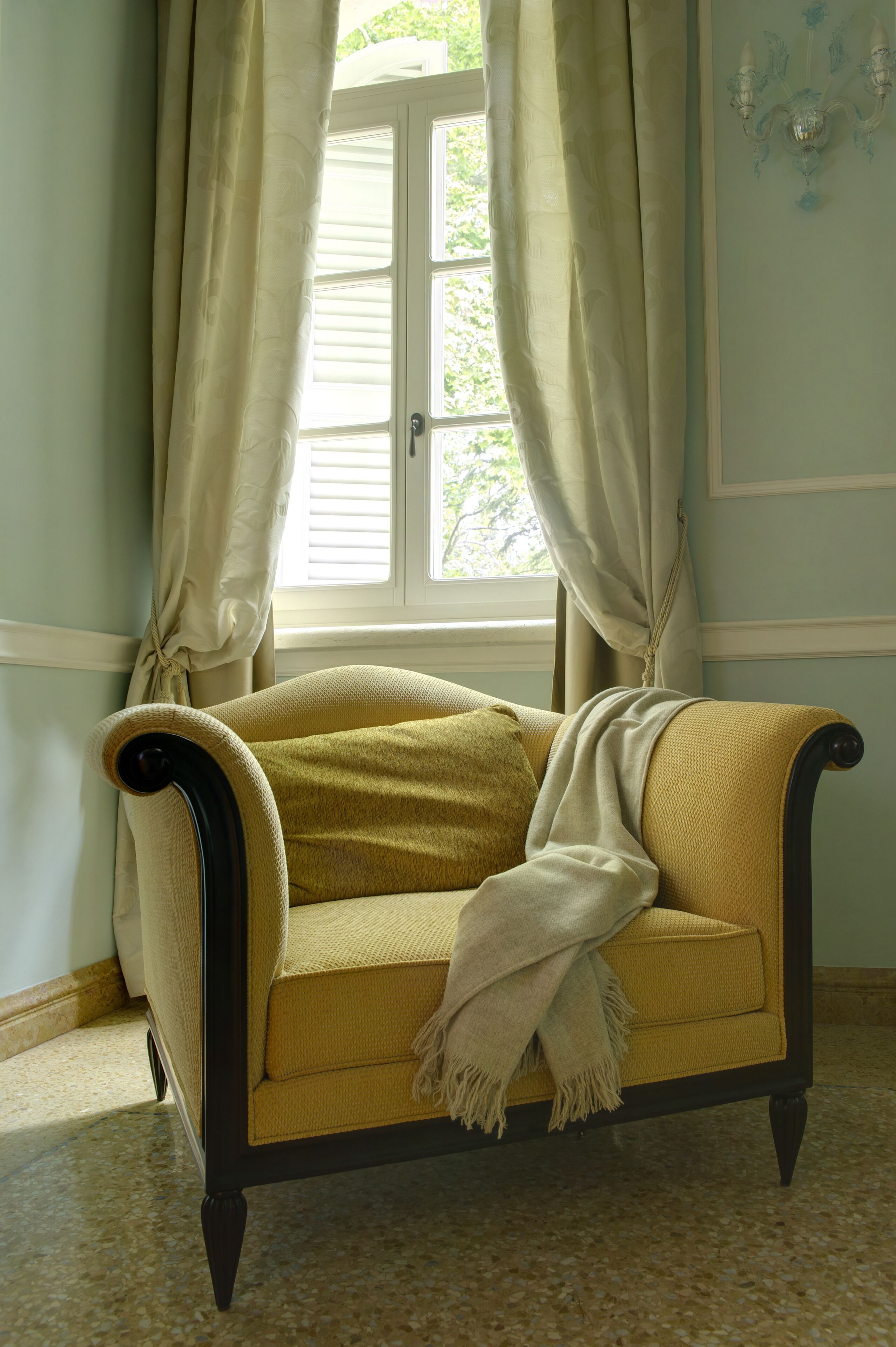 A room with a window, a chair, and a wall-mounted light fixture.
