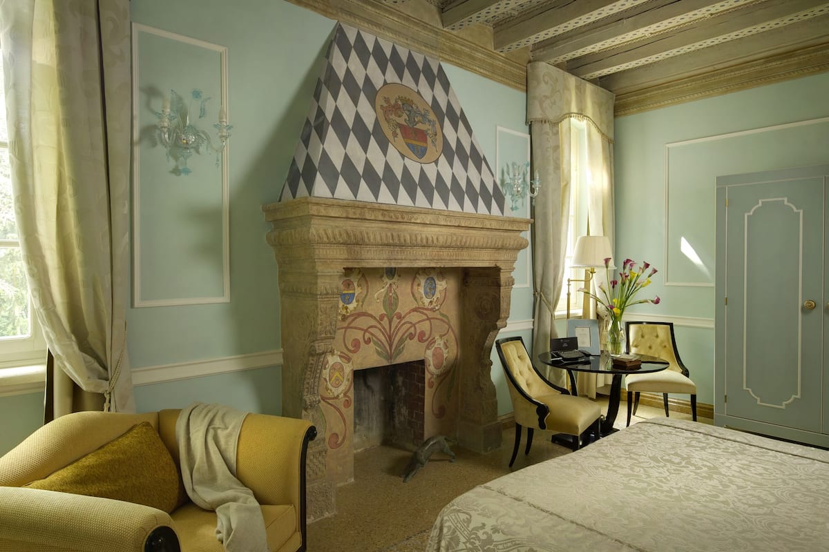 A room with a fireplace, a bed, a chair, a table, and a door.