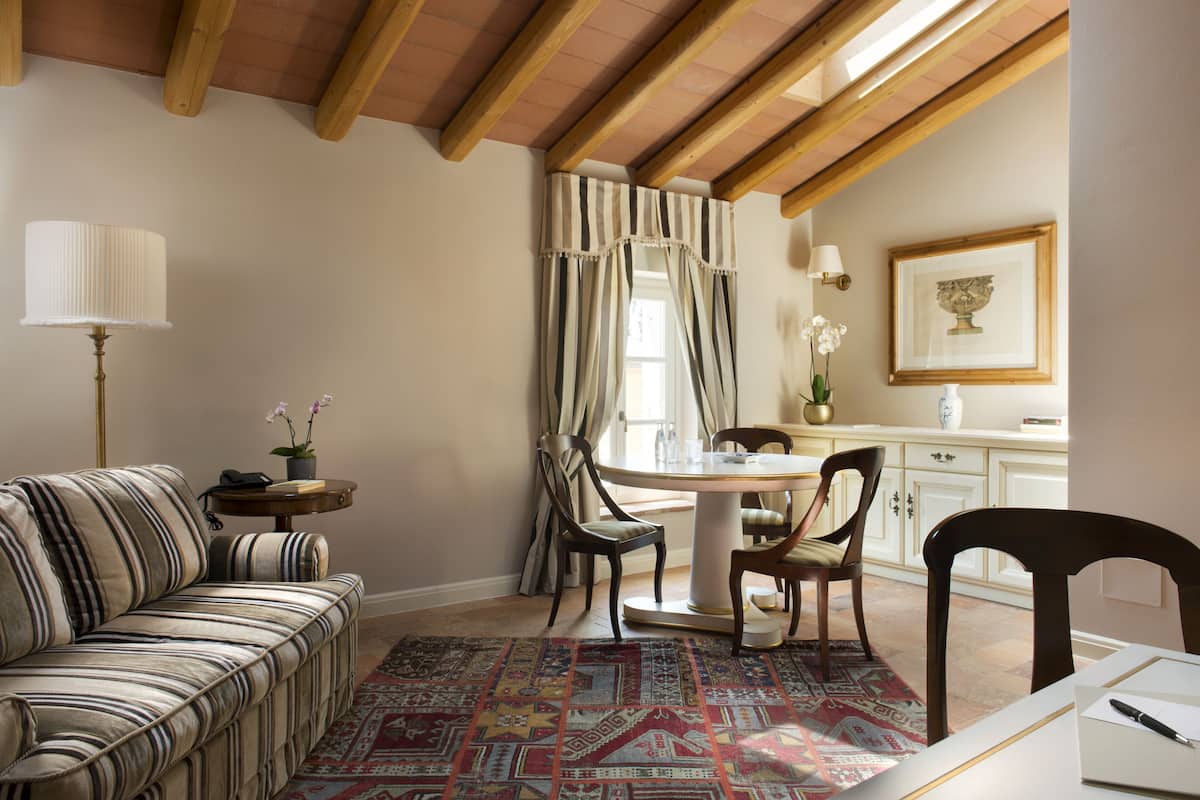 A dining area with a round table, chairs, a patterned rug, a striped sofa, and a lamp.
