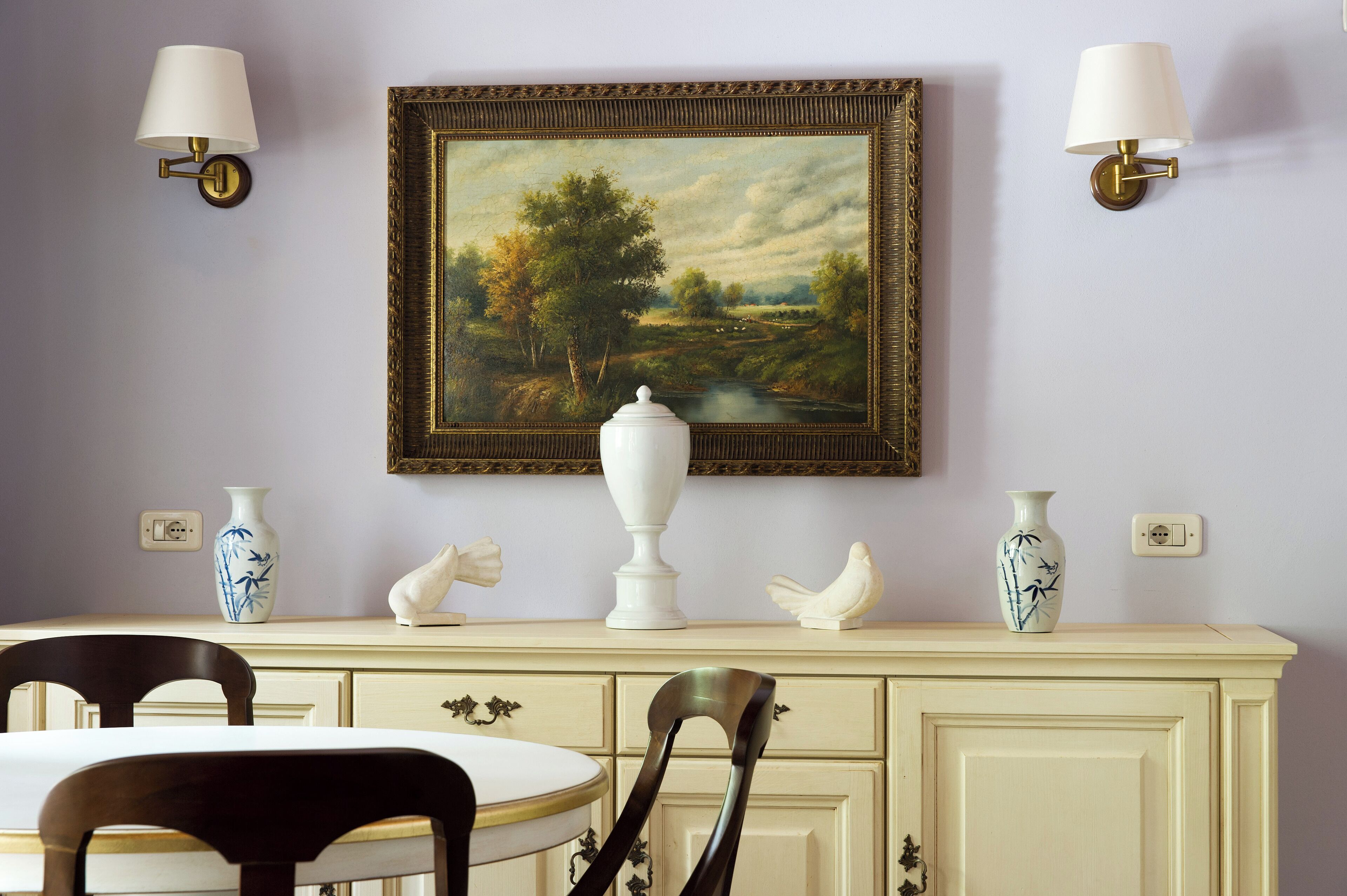 A dining area with a table, chairs, a cream-colored cabinet, and wall-mounted lamps.