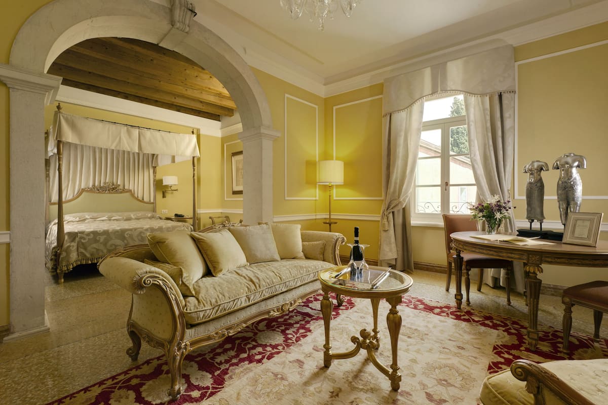 A room with a bed, a sofa, a dining table, and a chandelier.