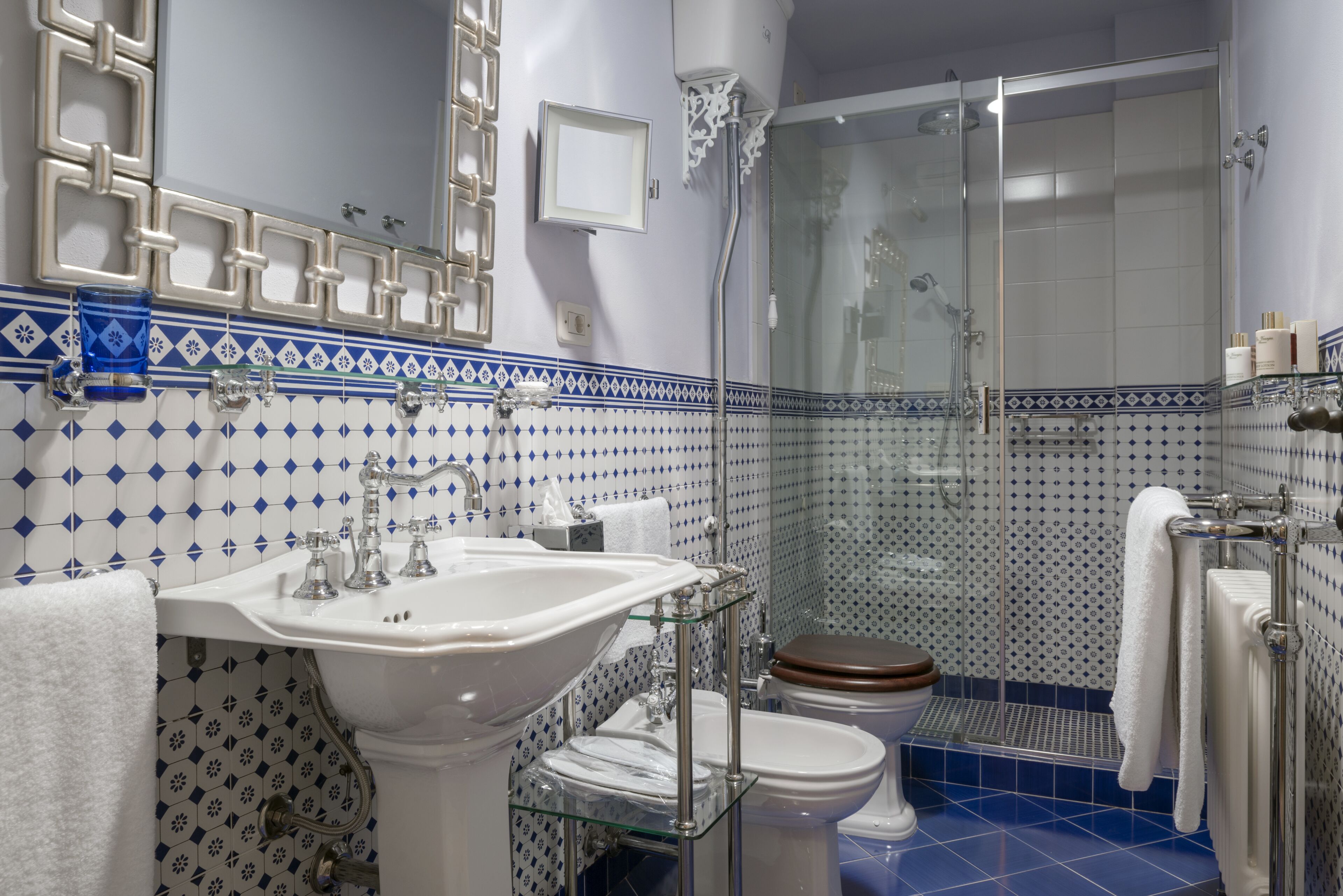 A bathroom with a glass shower enclosure, a white sink, a toilet, and a glass shelf.