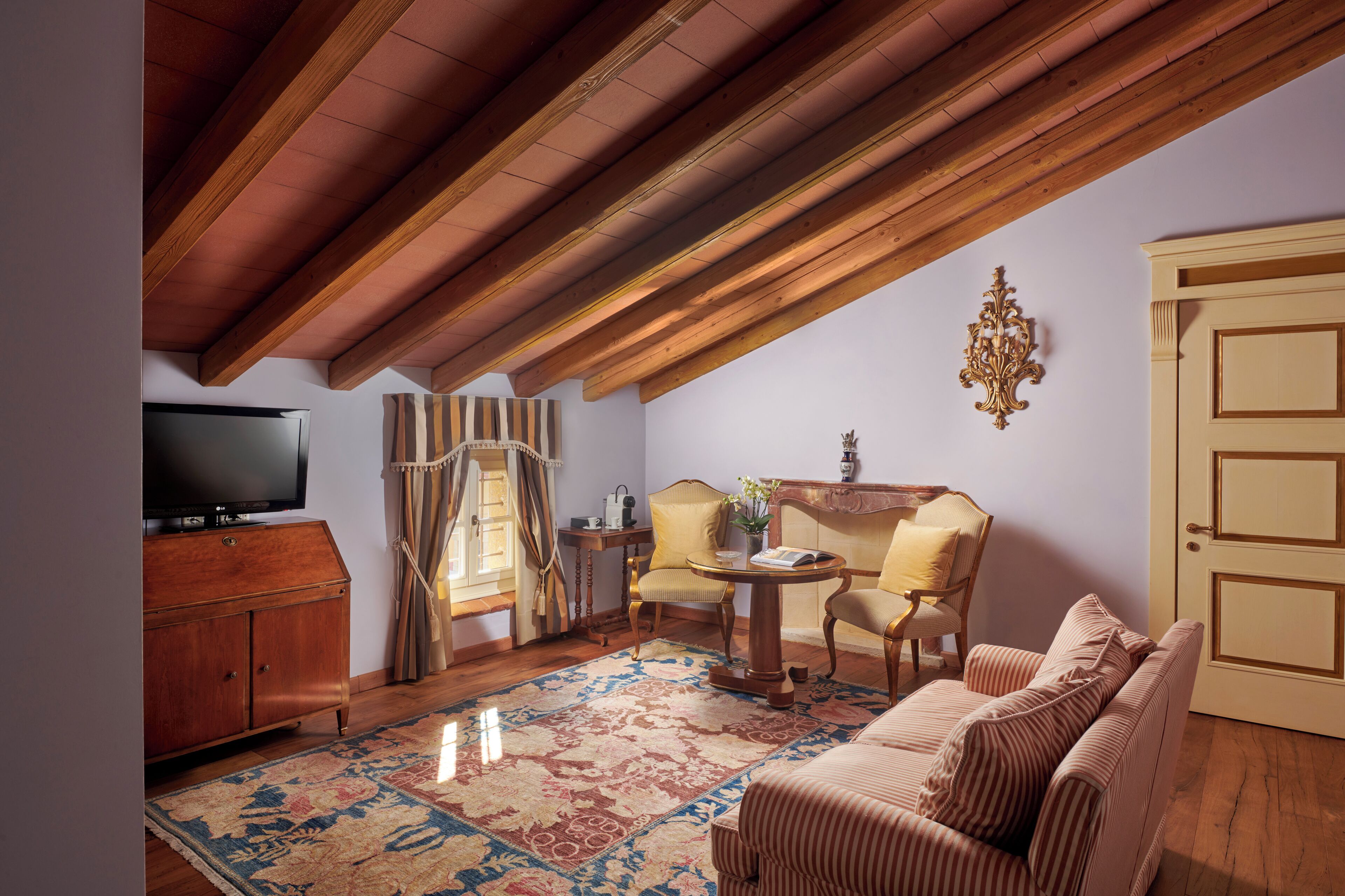 Una sala de estar acogedora con techo de madera, un televisor, una alfombra estampada, un sofá y una puerta.