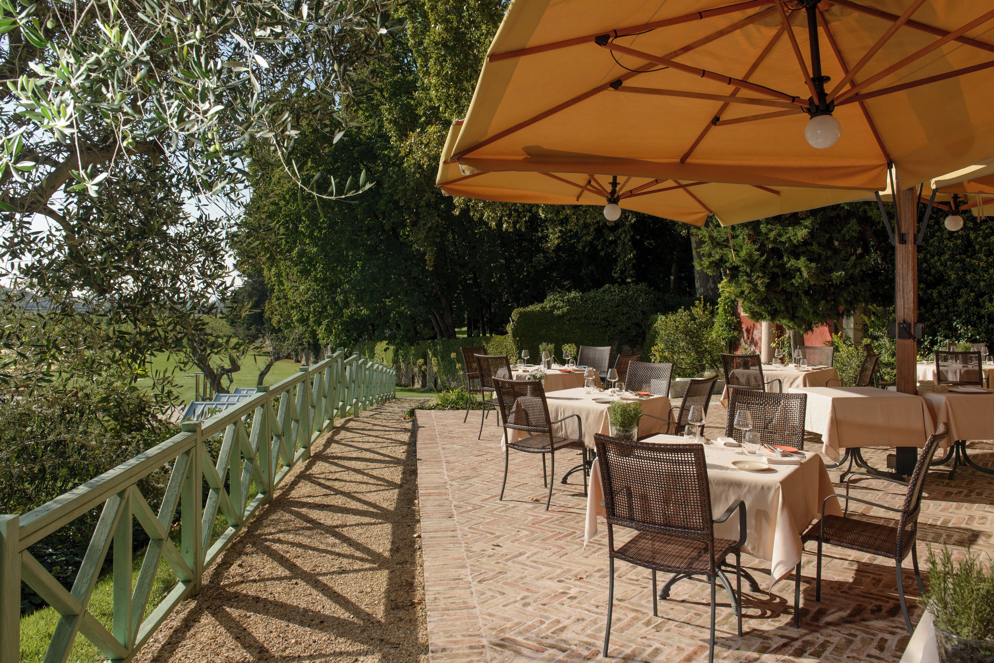 An outdoor patio with tables and chairs, surrounded by a wooden fence and greenery.