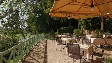 An outdoor patio with tables and chairs, surrounded by a wooden fence and greenery.