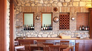 Zona de bar con paredes de piedra, botellas de vino expuestas en estanterías y una botellera.
