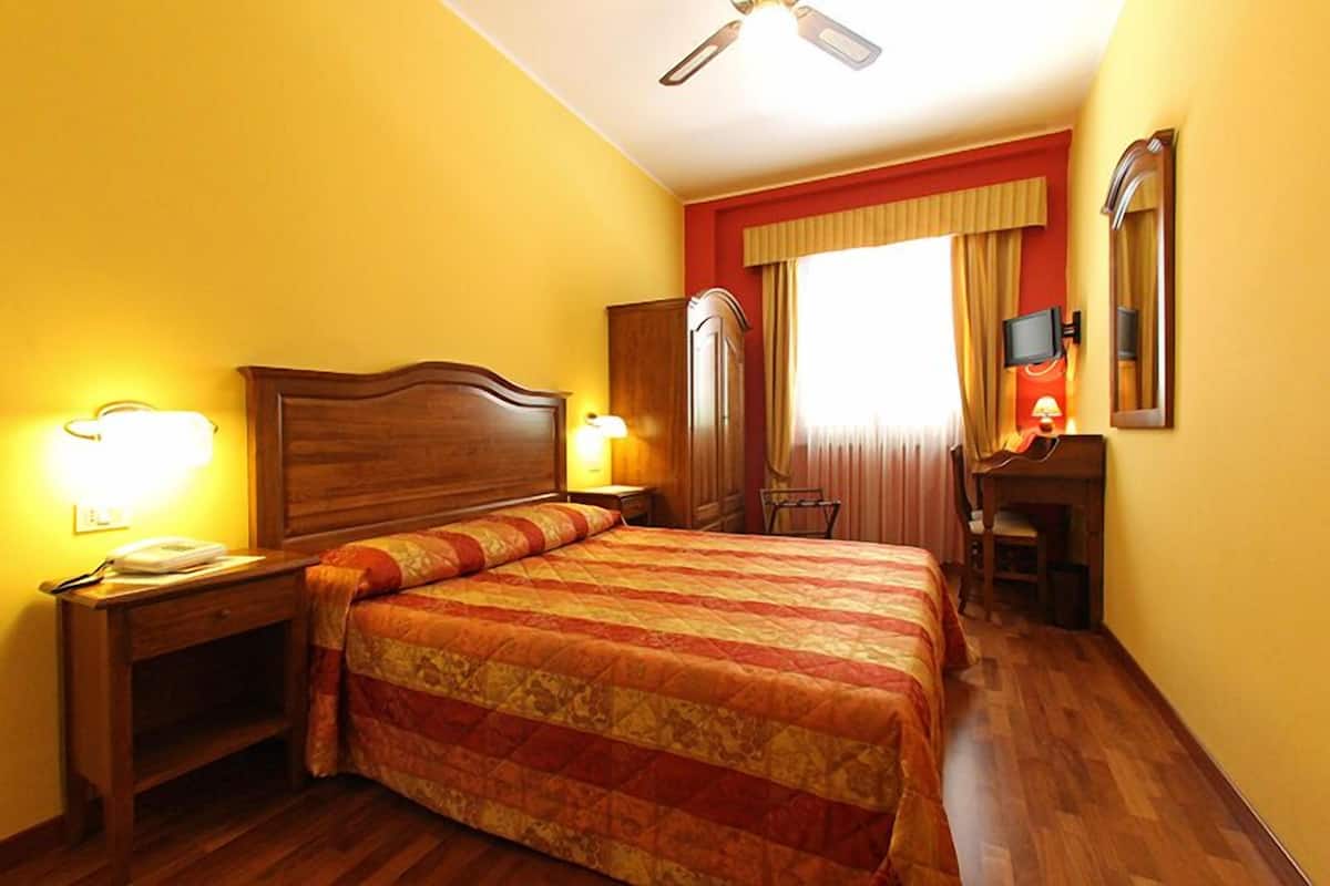 A hotel room with a wooden bed, bedside lamps, a desk with a chair, a television, and a mirror.