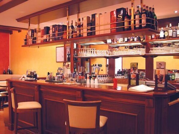 Zona de bar con varias estanterías llenas de botellas de licores y vasos, mostrador de bar de madera y taburetes.