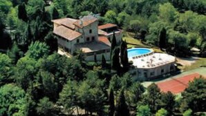 Vista aérea de una villa rodeada de un bosque denso, con piscina y una estructura de techo rojo cerca.