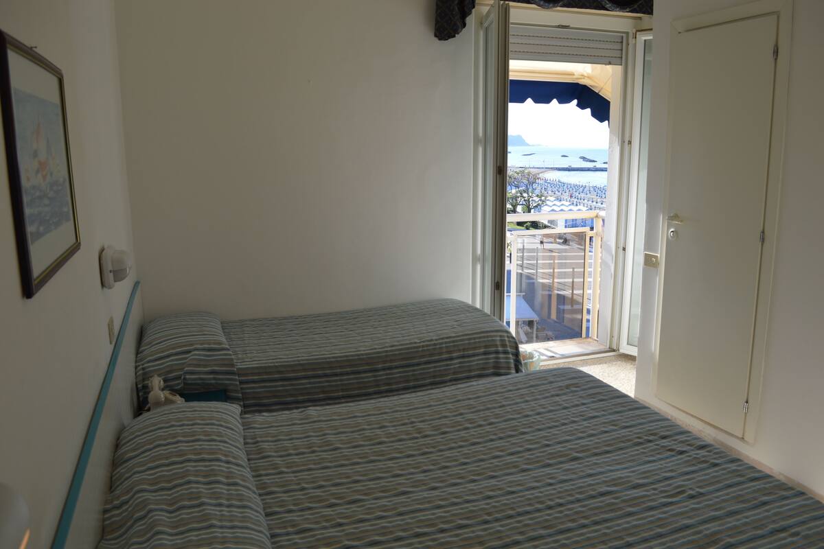 Una habitación con dos camas, una puerta y vista a una playa con sombrillas.