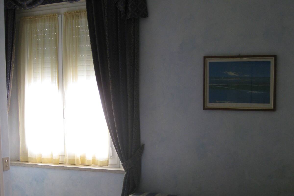 Una habitación con dos camas, una ventana con cortinas y un cuadro en la pared.