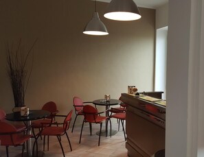 A dining area with a round table and red chairs, two pendant lights, and a vase with branches. - Hotel Amelia (Fano)