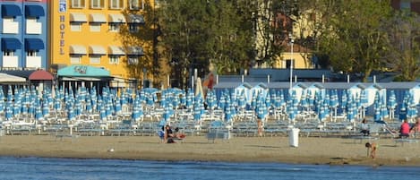 A beachside hotel with multiple balconies and a row of blue and white striped umbrellas.
