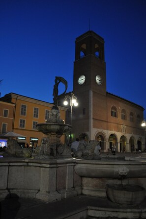 A historic building with a clock tower, a fountain, and a square with people. - Hotel Amelia (Fano)