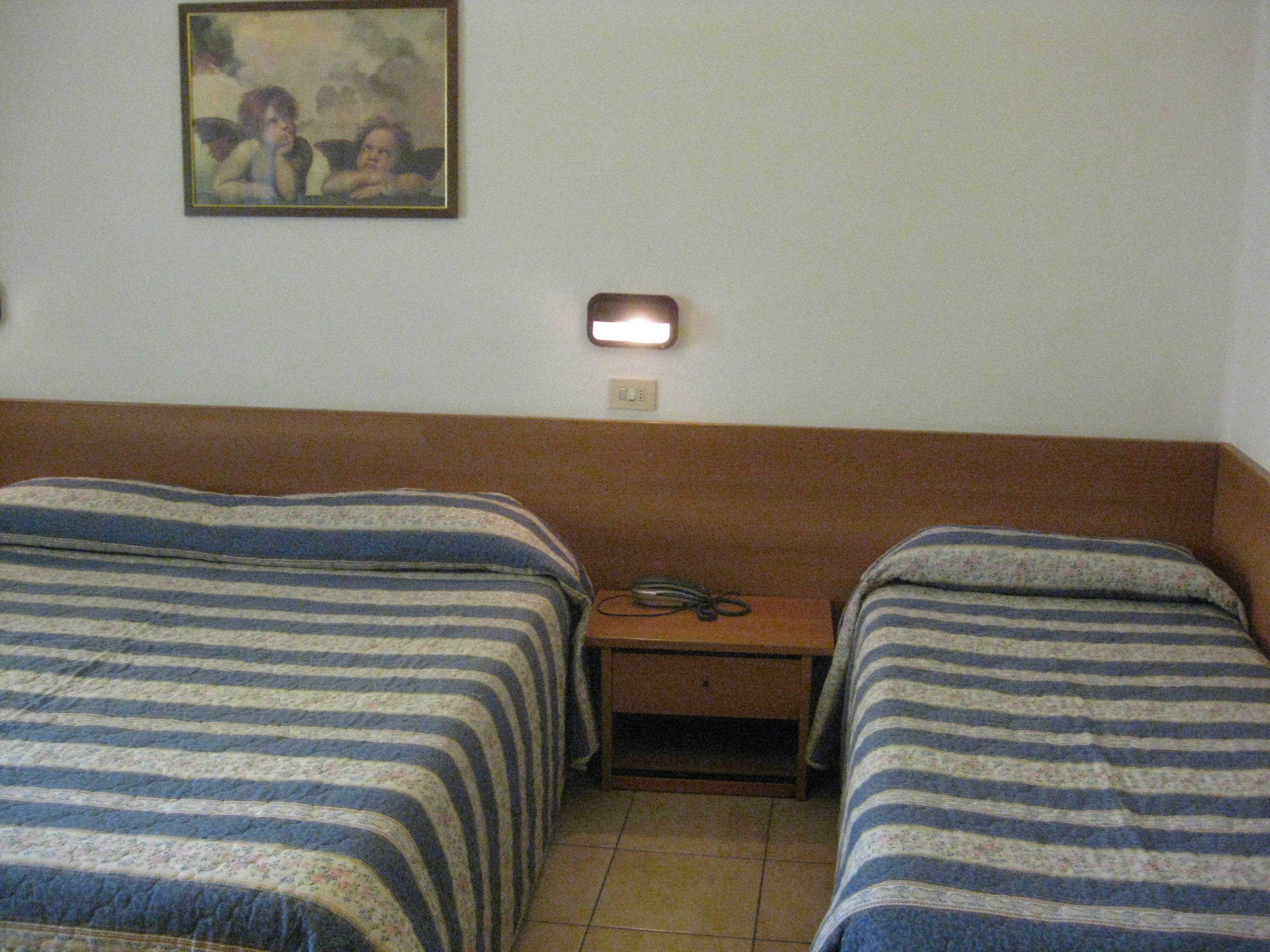 Een kamer met twee eenpersoonsbedden, een nachtkastje, een lamp en een schilderij aan de muur.