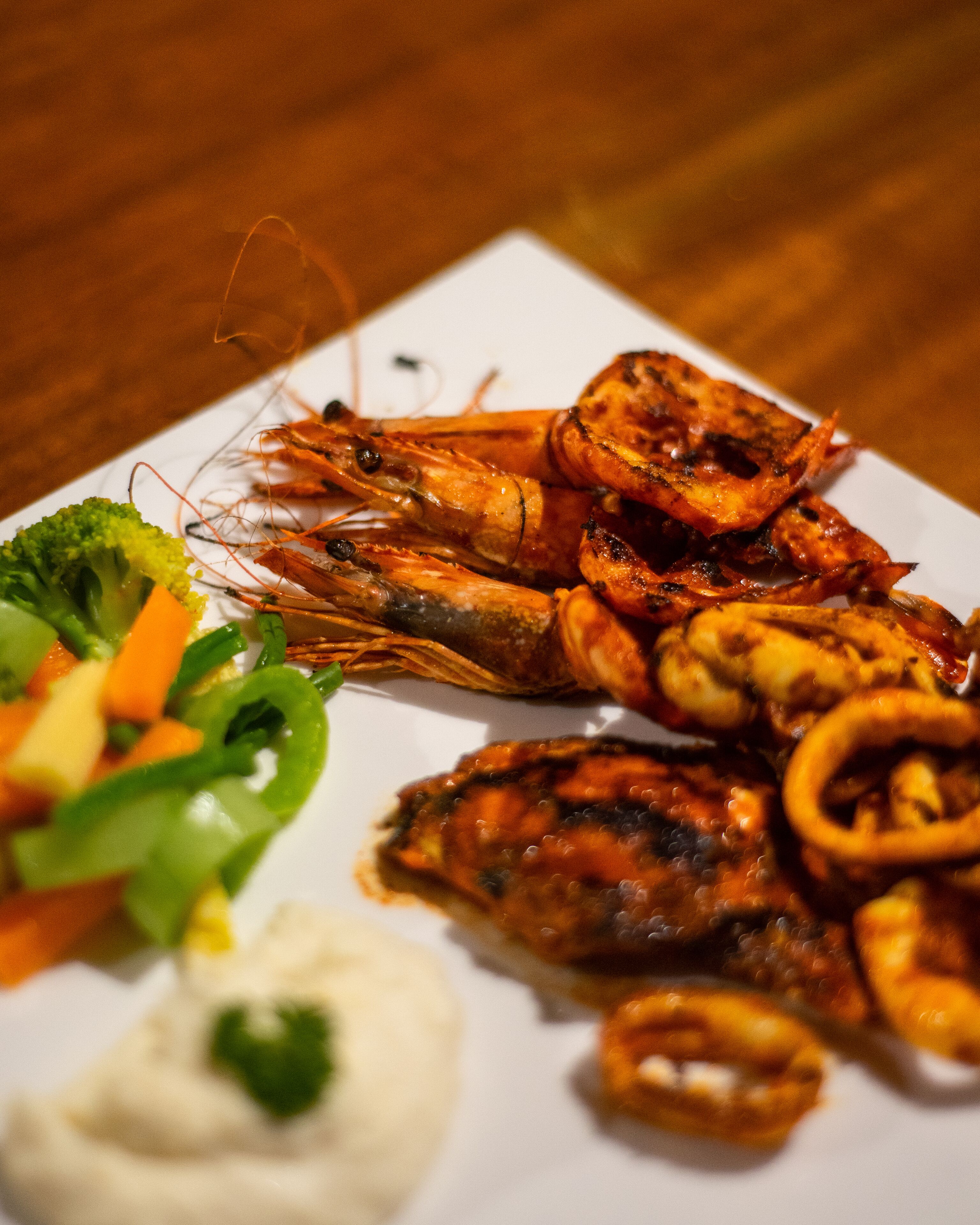 A plate of grilled shrimp with vegetables and a side of dipping sauce.