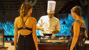 Um chef cozinha em um balcão, com dois clientes próximos.