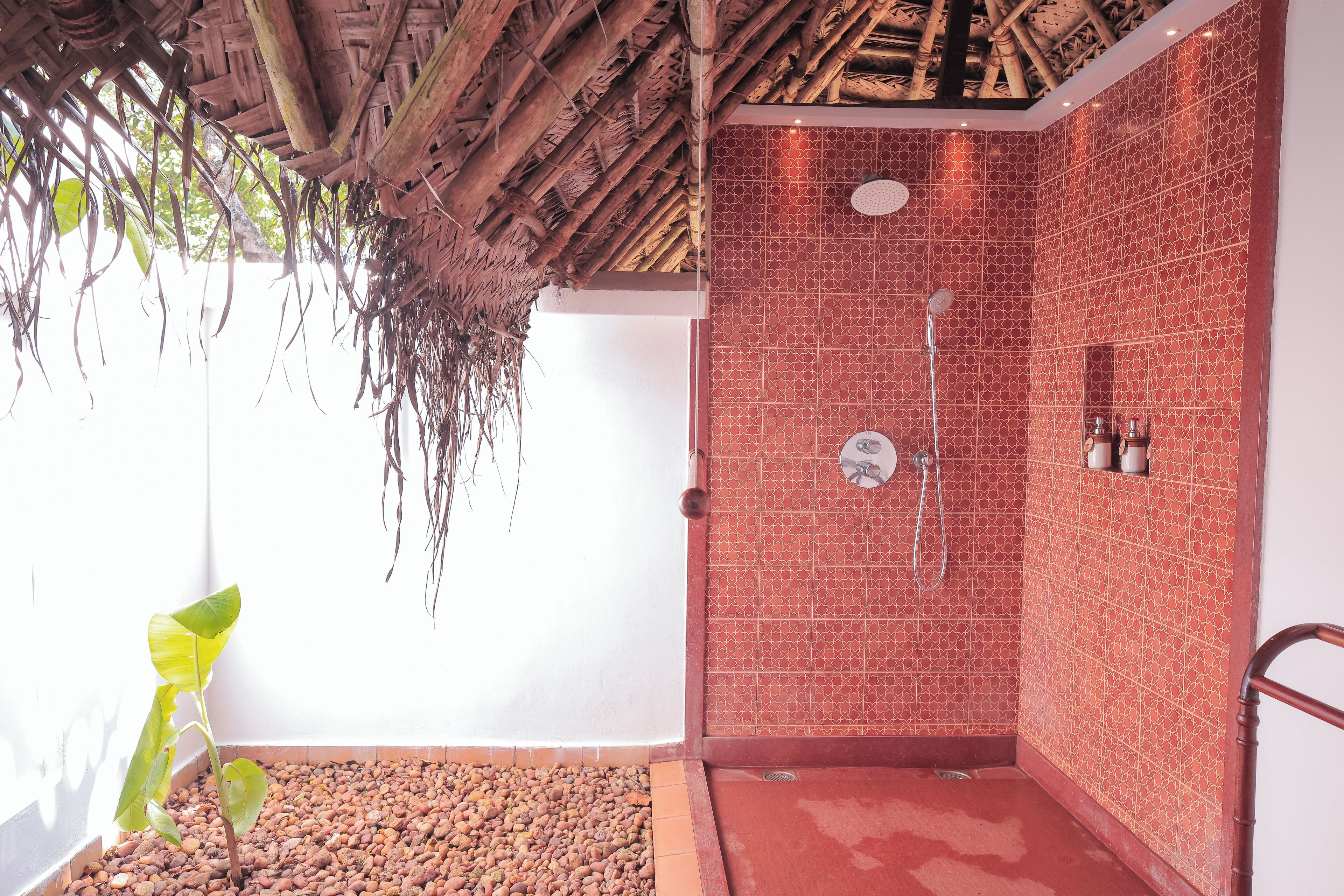 Un área de ducha con pared de azulejos rojos, techo de madera y una planta cerca de la ventana.