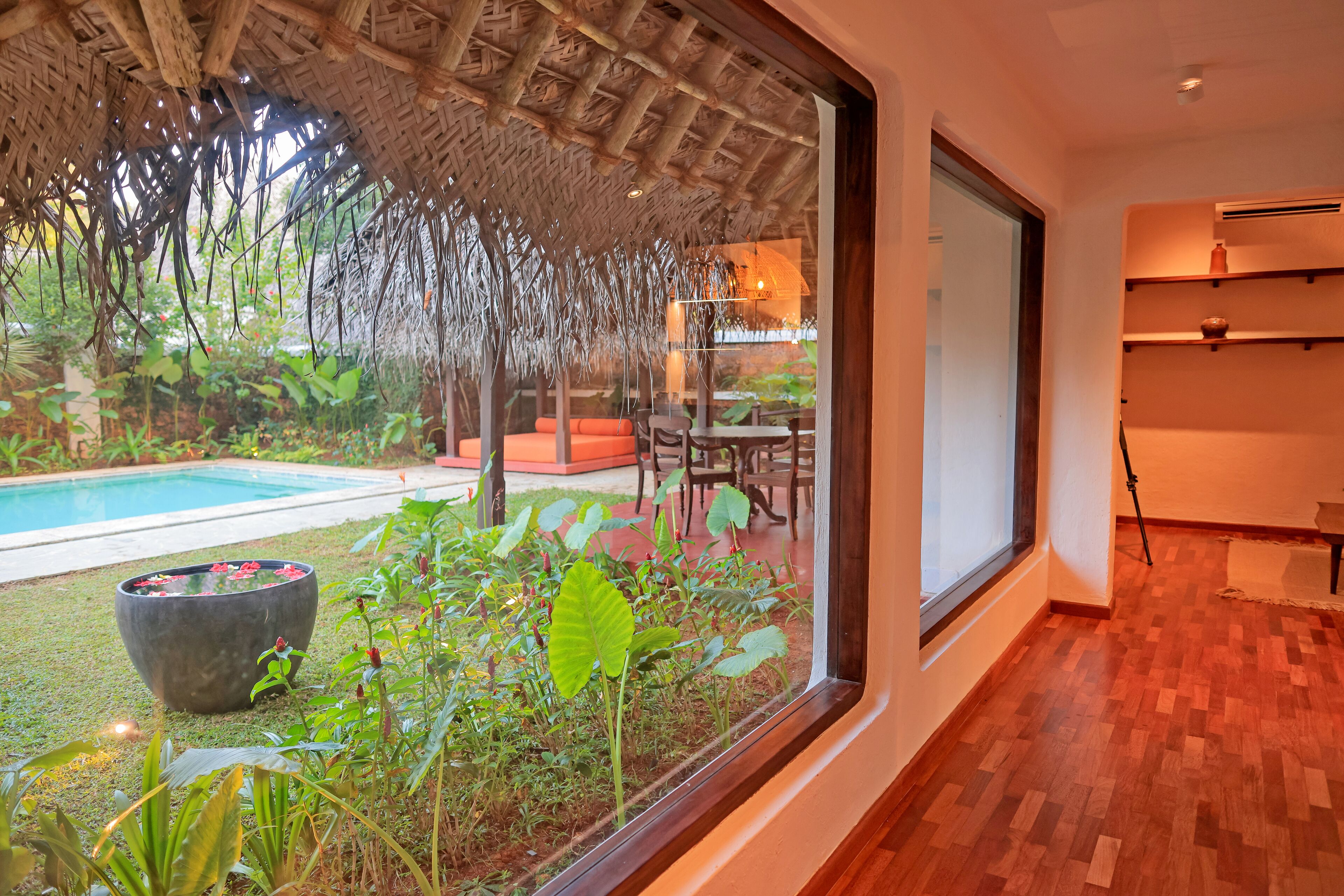Una habitación con un amplio ventanal que da a una piscina y un jardín exuberante.