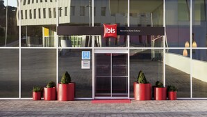 A modern hotel entrance with a glass facade, red planters, and a sign indicating it is an ibis hotel. - ibis Barcelona Santa Coloma (Santa Coloma de Gramenet)