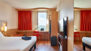 A hotel room with a bed, a desk, a TV, and a window with a city view. - ibis Barcelona Santa Coloma (Santa Coloma de Gramenet)