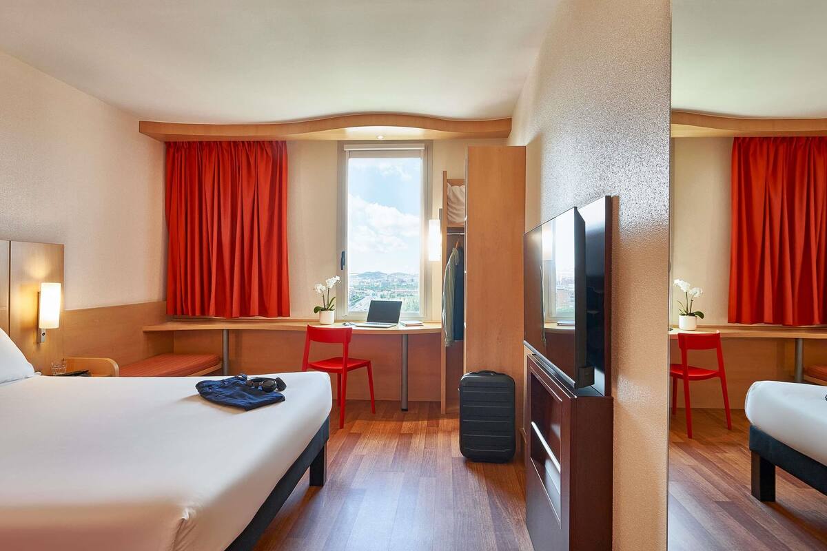 Habitación de hotel con cama, escritorio, televisión y ventana con vistas a la ciudad.