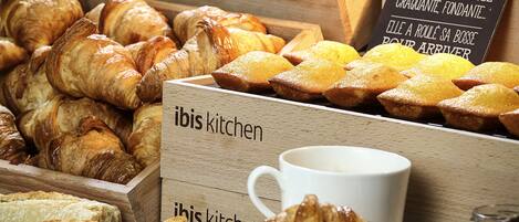 A variety of baked goods including croissants and muffins displayed in wooden boxes with a sign reading "Doree, Généréeuse, Graquante, Fondante".