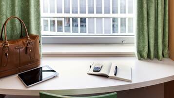 A room with a white desk, a brown leather handbag, a tablet, a notebook, and a pen.