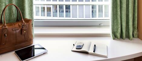 Une pièce avec un bureau blanc, un sac à main en cuir marron, une tablette, un carnet et un stylo.