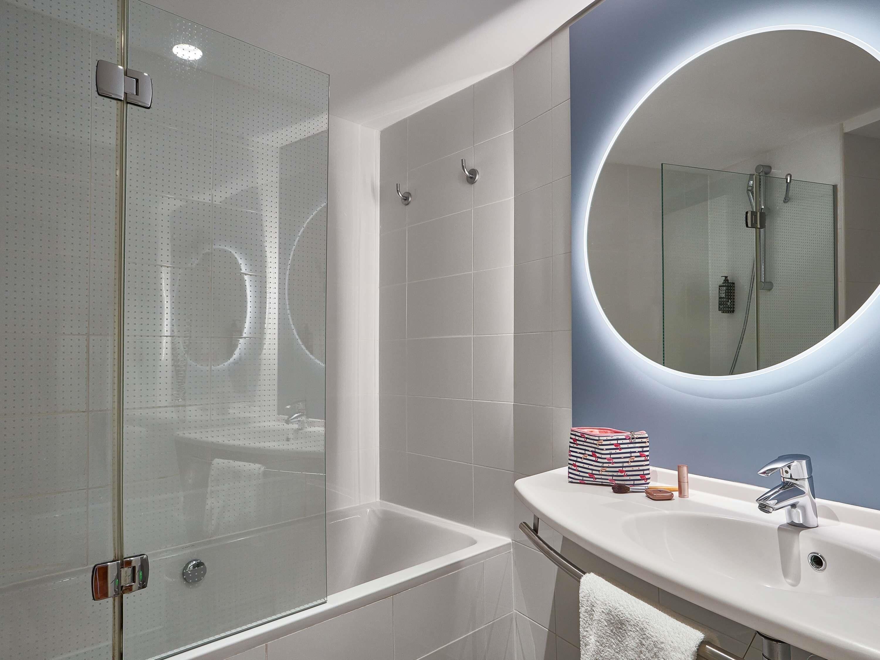 A modern bathroom with a glass shower enclosure, a white bathtub, and a vanity with a mirror.