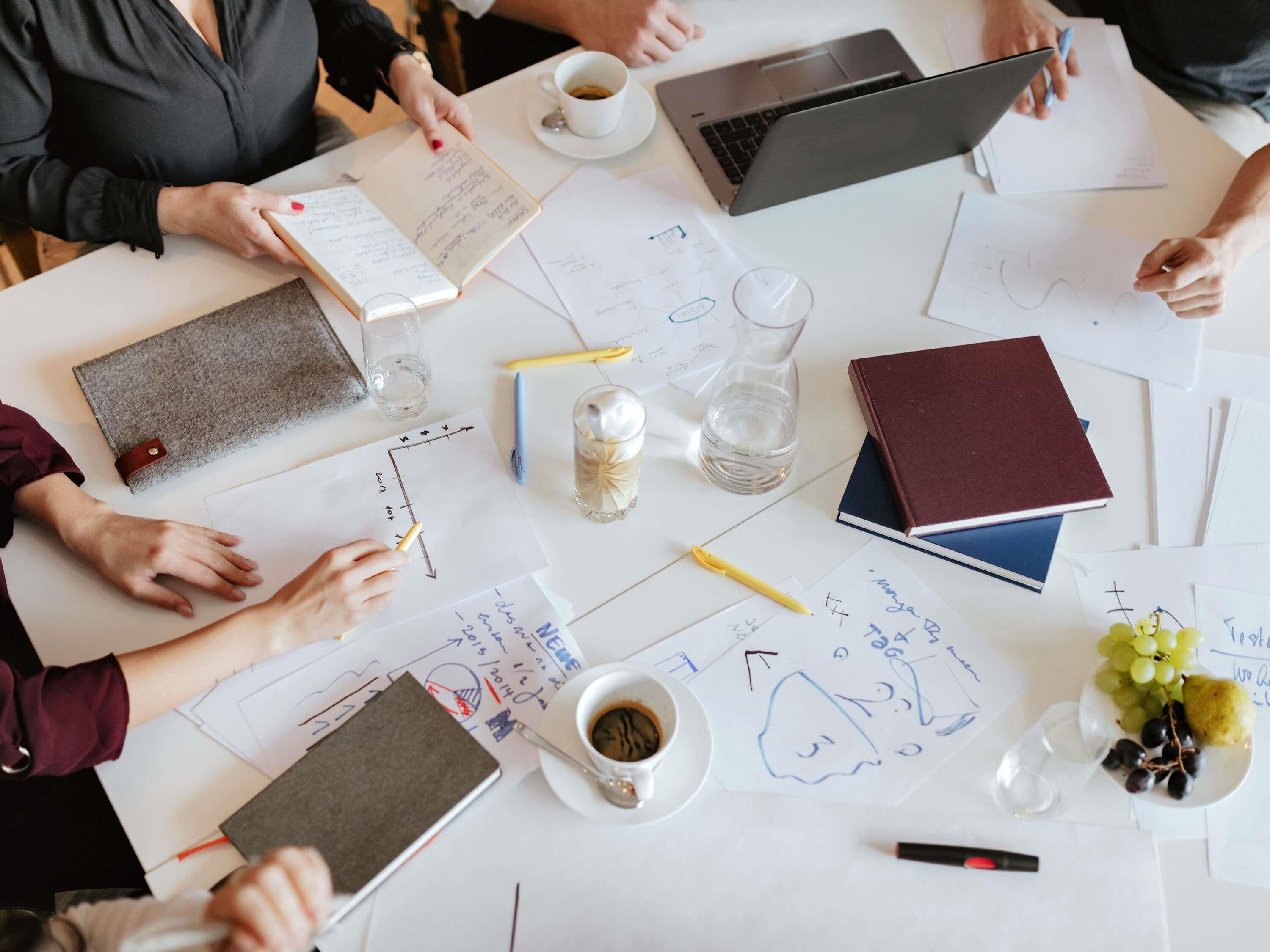 Una reunión con documentos, computadoras portátiles y una taza de café sobre una mesa.