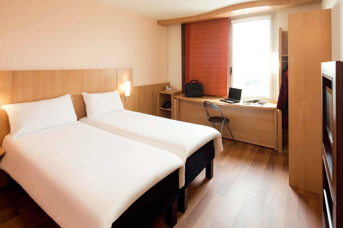 Una habitación de hotel con dos camas, un escritorio con una computadora portátil, una silla y un televisor.