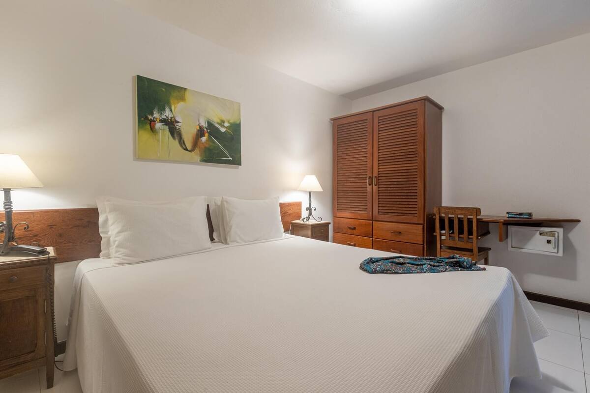 Ein Hotelzimmer mit einem Bett, zwei Nachttischen, einem Holzschrank, einem Schreibtisch mit Stuhl und einem Bild an der Wand.