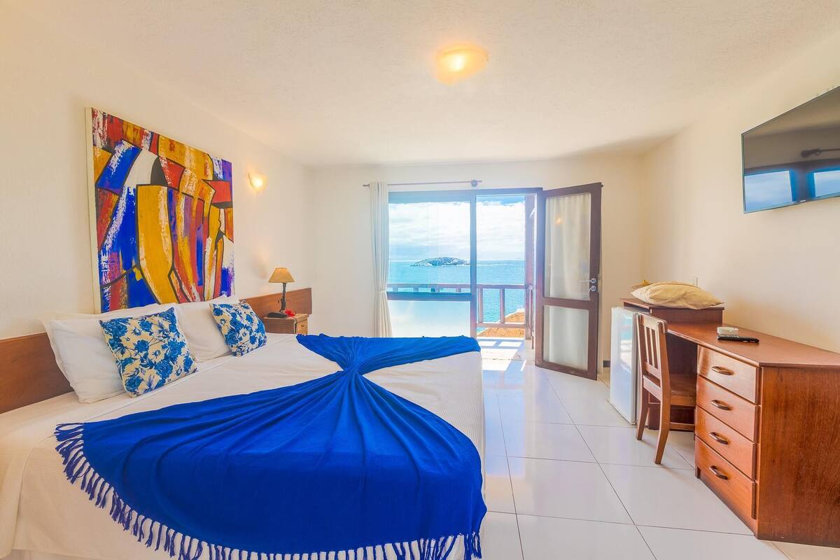 Ein Hotelzimmer mit Bett, Schreibtisch, Stuhl, Fernseher und einem Balkon mit Meerblick.