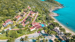 Vista aérea de un complejo turístico en la costa con varias edificaciones, una piscina y una playa.