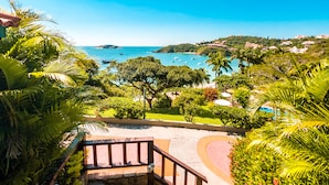 Una escalera conduce a un área de piscina rodeada de exuberante vegetación y vistas al mar.