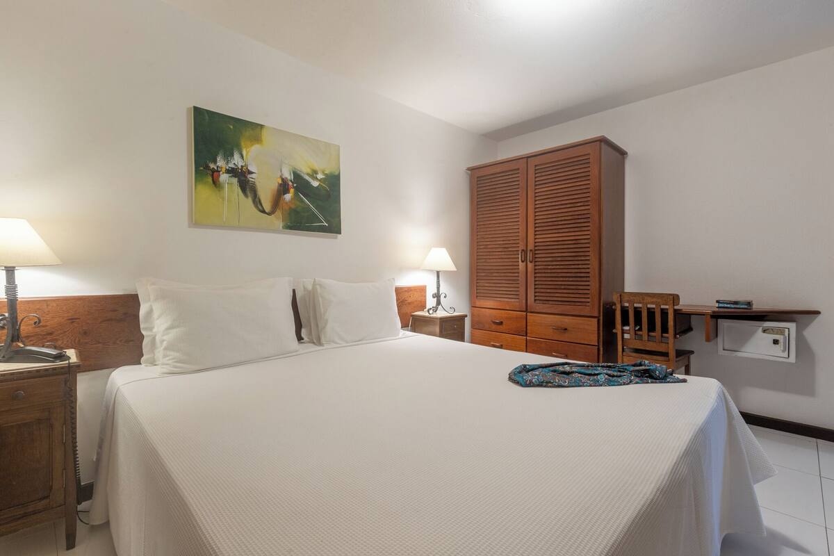 Ein Hotelzimmer mit einem Bett, zwei Nachttischen mit Lampen, einem Holzschrank und einem Gemälde an der Wand.