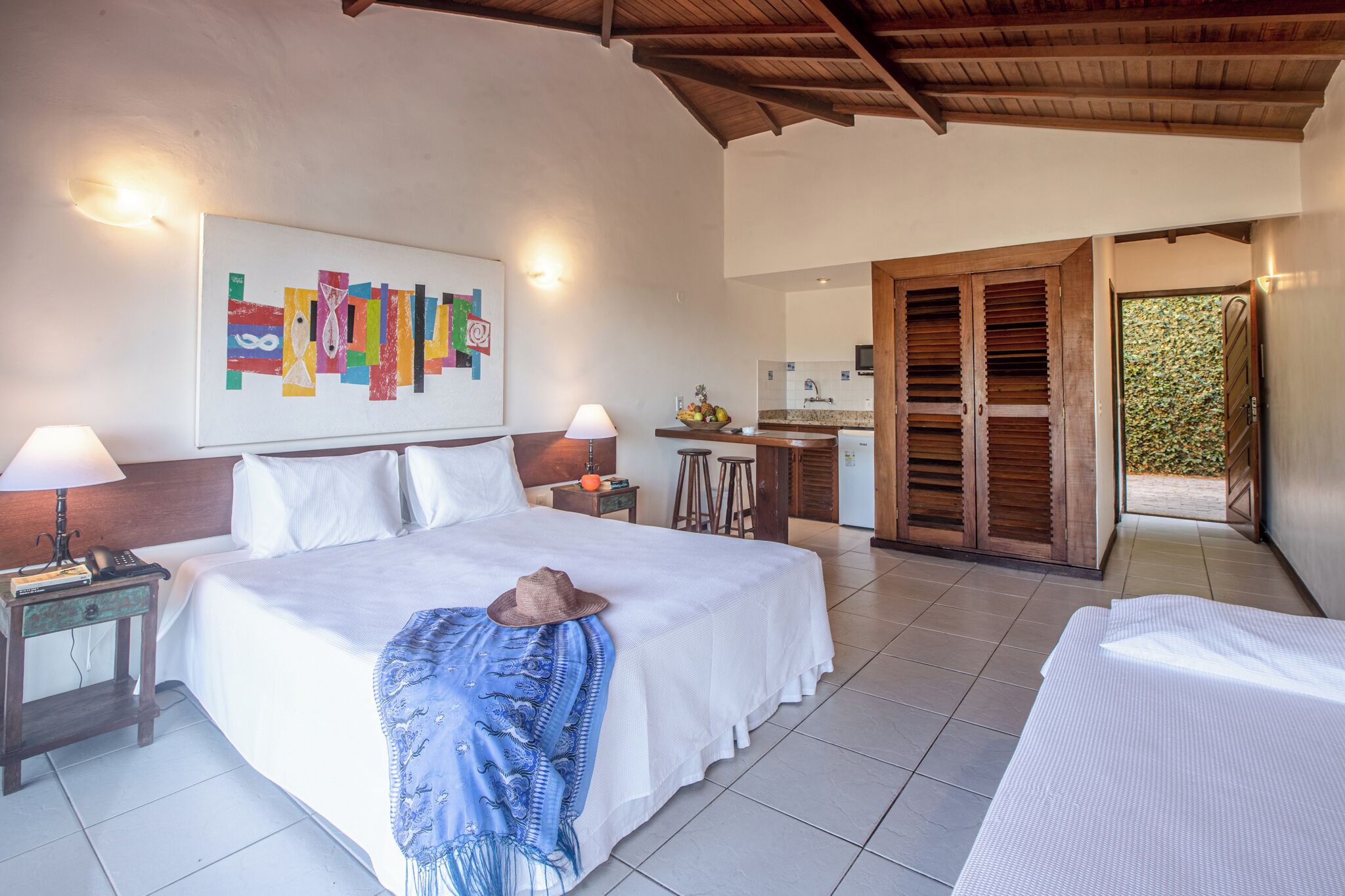 Hotelkamer met een bed, nachtkastjes, een lamp, een kunstwerk aan de muur en uitzicht op de keuken en buiten.