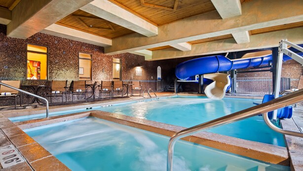 An indoor pool with a blue slide, seating area, and a brick wall. - Best Western Plus KC Speedway Inn & Suites (Kansas City)